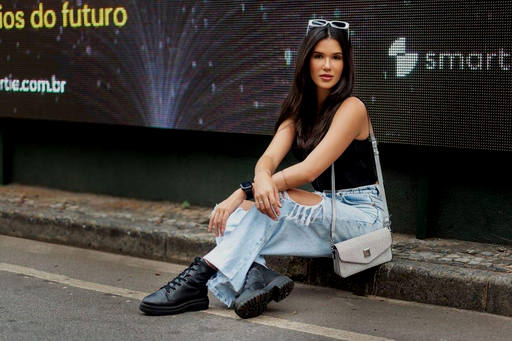 Mulher usando calça jeans sentada meio fio da calçada.