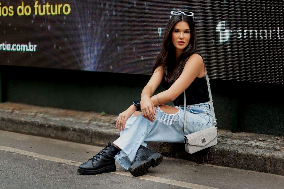 Mulher usando calça jeans sentada meio fio da calçada.